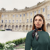 Woman in a green sweater with a patterned scarf standing in front of a large architectural building.